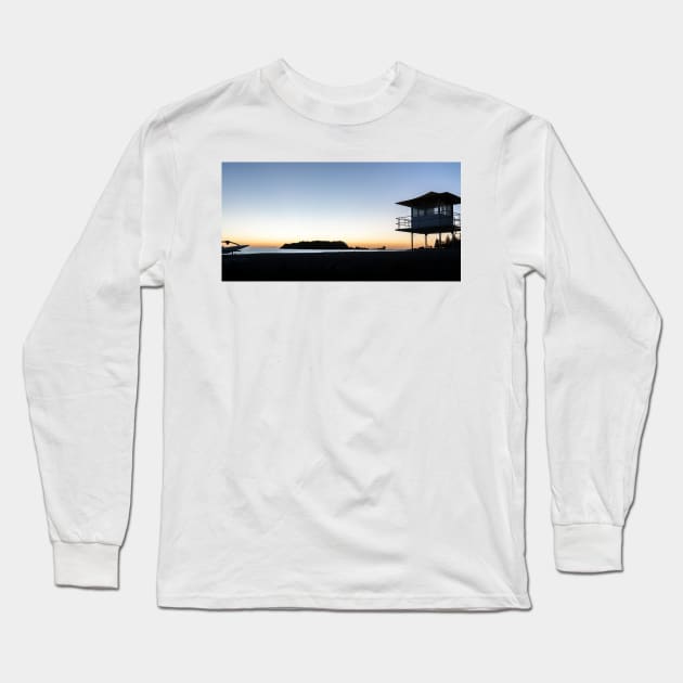 Silhouetted against golden glow of sunrise lifesafers lookout on Mount Maunganui beach New Zealand. Long Sleeve T-Shirt by brians101